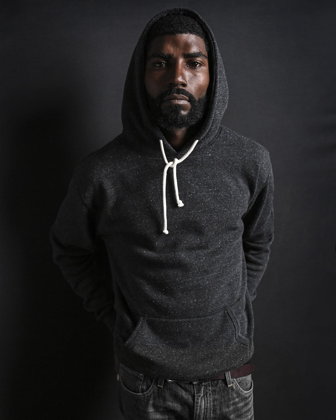 Man in a white t-shirt and necklace, standing against a dark background.